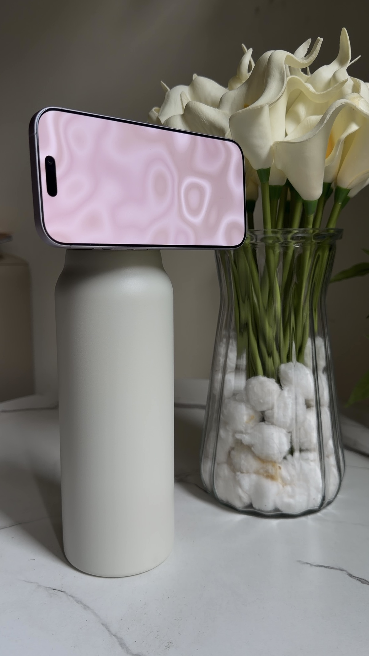 Cream White SANNI bottle supporting a phone beside white flowers