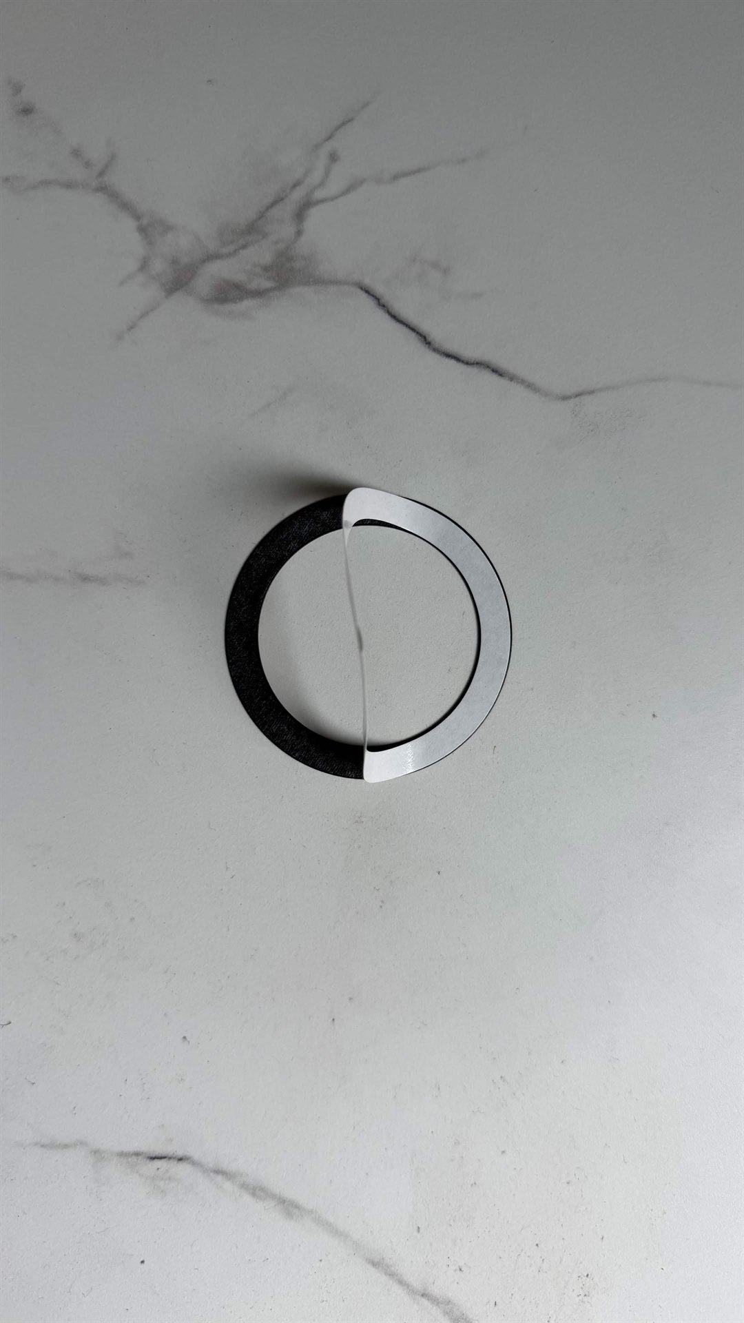 White protective backing being peeled from the black MagSafe adapter ring