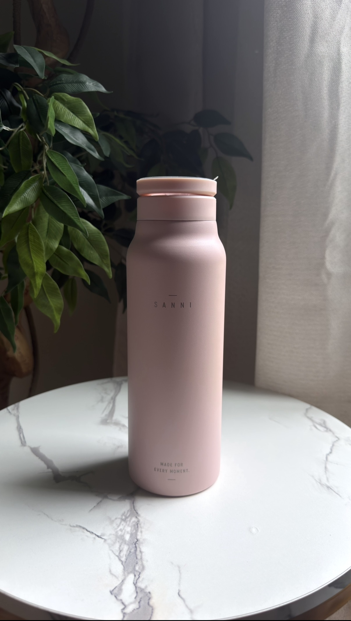 Pink SANNI bottle with its lid open beside a window
