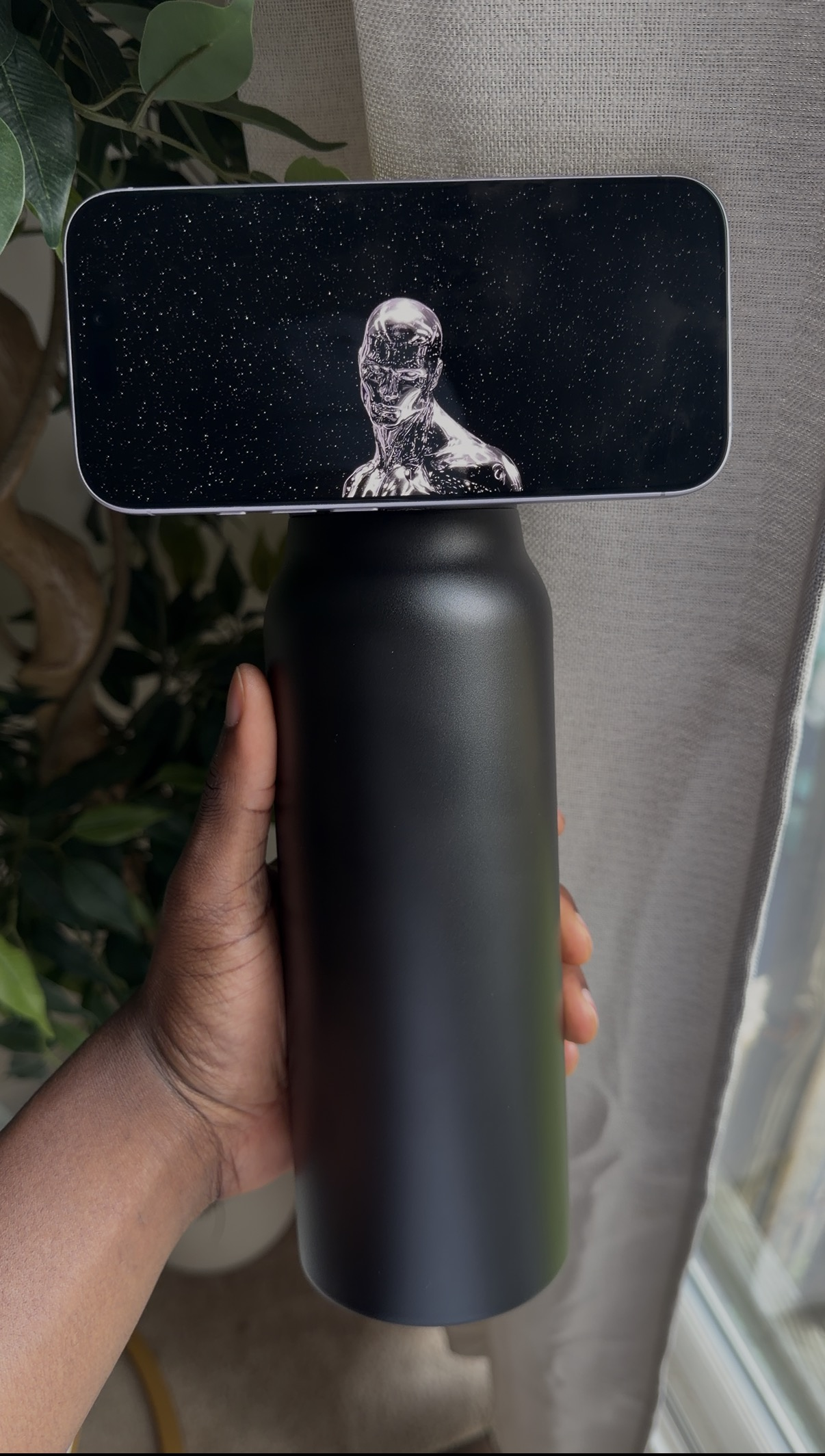 Black SANNI bottle holding a phone beside a window